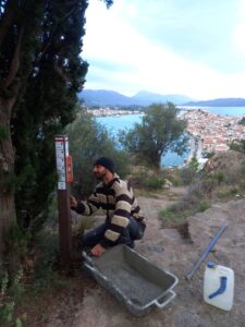 Antonis Panou from Paths of Greece installing a recycled plastic pole with hiking directions with the town of Poros at the background