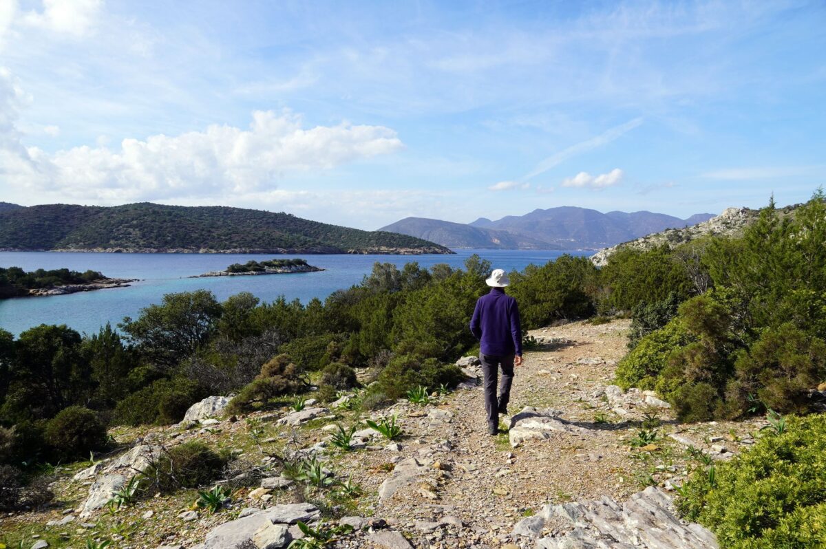 A hiker with a hat walking on Poros Trails with sea at the background