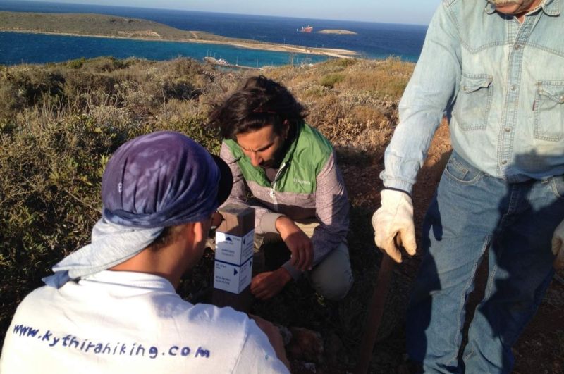 People installing a sign with directions on a trail near Diakofti, Kythera with the sea at the background.
