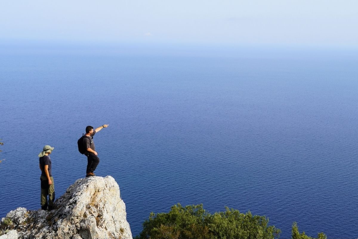 A local person pointing to a trail to a Paths of Greece member on Skiathos, with sea at the background