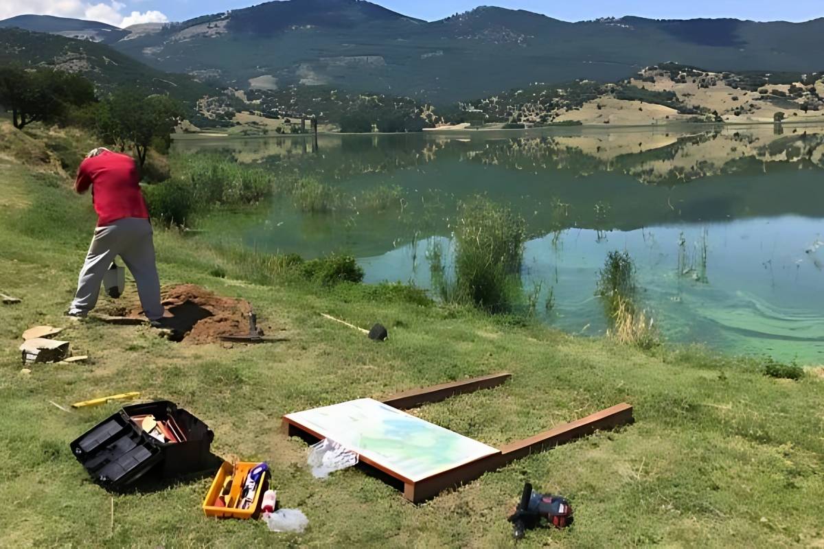 A person installing a trailhead sign with lake Zazari at the background