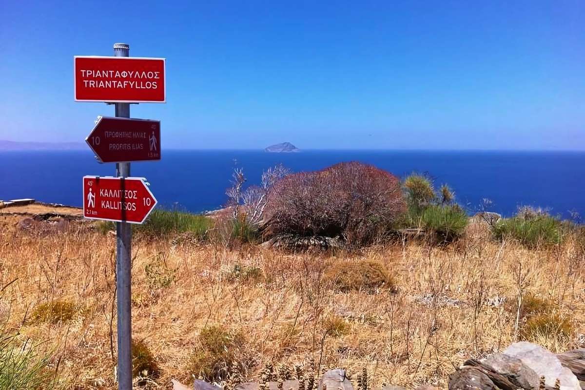 Red metallic directional signs with the sea at the background on the island of Serifos